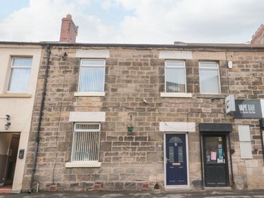 Stone facade of a building with a blue door and windows a vape bar on the right at Victoria Cottage in Amble