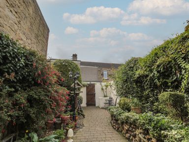 A garden pathway with plants pots and outdoor seating at Victoria Cottage in Amble