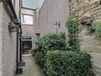 A narrow outdoor passageway with brick paving stone walls plants and a window at Victoria Cottage in Amble