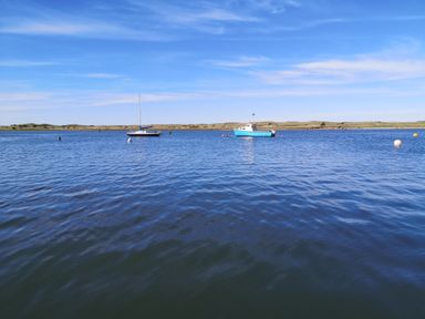 A body of water with two boats and buoys with land and a blue sky in the background at Victoria Cottage in Amble