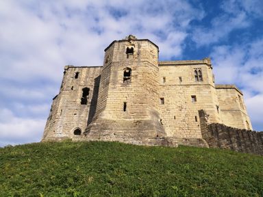 A stone castle on a grassy hill under a blue sky with clouds at Victoria Cottage in Amble