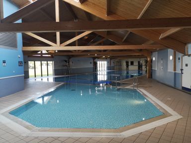 An indoor swimming pool area with wooden beams on the ceiling and two connected pools at Victoria Cottage in Amble