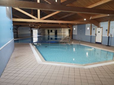 An indoor swimming pool area with wooden ceiling beams and tiled floor at Victoria Cottage in Amble