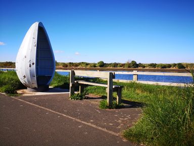 A wooden bench and a white boat turned upright by a river with grass and a wooden fence nearby at Victoria Cottage in Amble