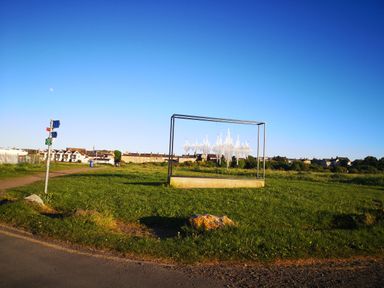 An outdoor art installation on a grassy field near a path with houses in the background at Victoria Cottage in Amble