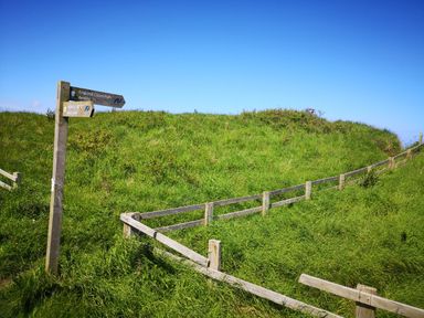 A grassy hillside with a wooden signpost and a wooden fence under a blue sky at Victoria Cottage in Amble