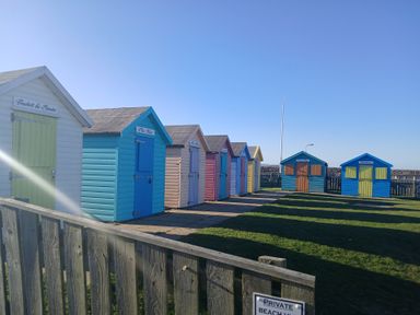 A row of colorful beach huts with a wooden fence in front at Victoria Cottage in Amble