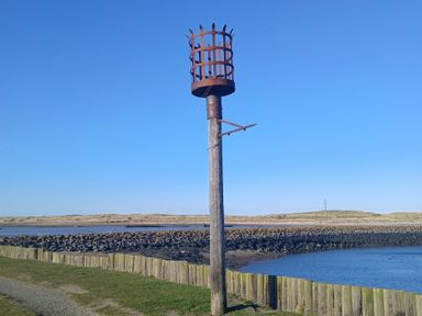 A wooden post with a metal cage structure on top near a body of water with a rocky shoreline and a clear sky at Victoria Cottage in Amble