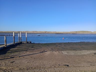A sandy shore with wooden posts and a body of water with buoys and sand dunes in the background at Victoria Cottage in Amble