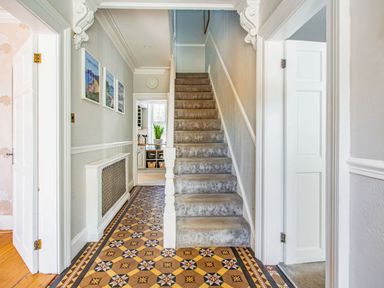 A hallway with patterned tiled floor leading to carpeted stairs and doors to adjacent rooms at Bryn Rhosyn in Nefyn