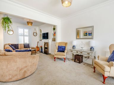 A living room with beige sofas a TV on a white cabinet and a console table with two lamps at Bryn Rhosyn in Nefyn