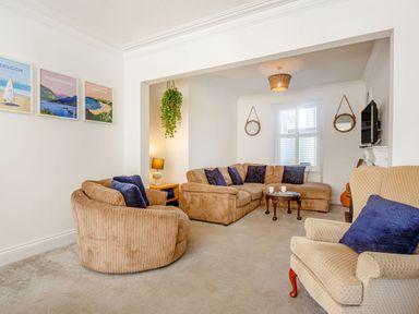 A living room with beige sofas and armchair with blue cushions a wooden coffee table hanging plant and framed prints on the wall at Bryn Rhosyn in Nefyn