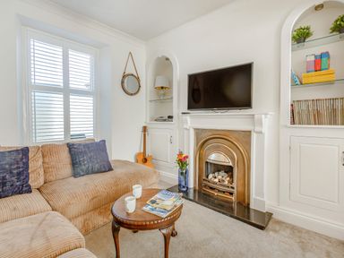 A living room with a beige sofa a wooden coffee table a guitar on the corner a fireplace with a TV above and built-in shelves at Bryn Rhosyn in Nefyn