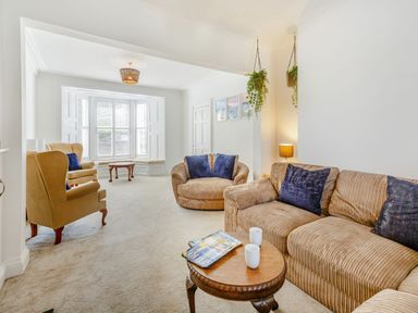 A living room with beige sofas, armchairs, hanging plants, and a round wooden coffee table at Bryn Rhosyn in Nefyn