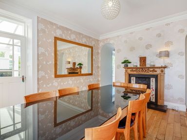 A dining room with a glass table and wooden chairs near a fireplace and large mirror at Bryn Rhosyn in Nefyn