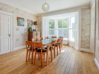 A dining room with a wooden table and eight chairs near a bay window at Bryn Rhosyn in Nefyn