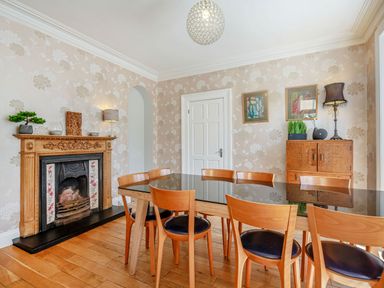 A dining room with a wooden table and six chairs a decorative fireplace and wooden cabinet at Bryn Rhosyn in Nefyn