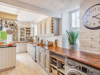A kitchen with cream cabinets wooden countertops hanging pots a wall clock and a washing machine at Bryn Rhosyn in Nefyn