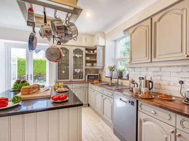 A kitchen with hanging pots and pans a countertop with fresh vegetables and bread and cabinets with dishes at Bryn Rhosyn in Nefyn