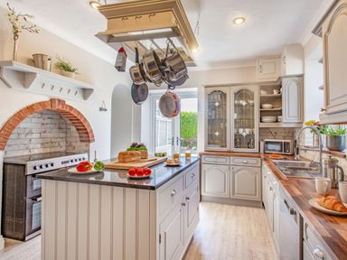 A kitchen with an island counter hanging pots and pans a stove with a brick arch and cupboards with dishes at Bryn Rhosyn in Nefyn