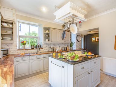 A kitchen with hanging pots and pans an island with vegetables and bread and a window with plants at Bryn Rhosyn in Nefyn