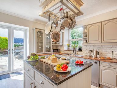 A kitchen with hanging pots pans an island with vegetables and bread near glass doors at Bryn Rhosyn in Nefyn