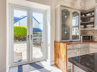 A kitchen with glass cabinet doors wooden countertops a microwave and patio doors leading outside at Bryn Rhosyn in Nefyn