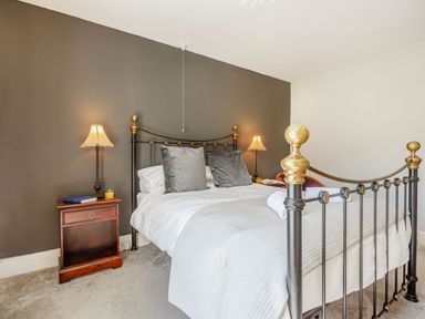 A bedroom with a metal bed frame two lamps on nightstands and gray accent wall at Bryn Rhosyn in Nefyn