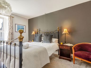 A bedroom with a metal bed a nightstand with lamps and a chair at Bryn Rhosyn in Nefyn