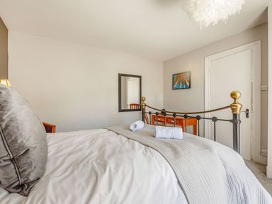 A bedroom with a metal bed frame two rolled towels on the bed a wooden dresser a mirror on the wall and a painting at Bryn Rhosyn in Nefyn