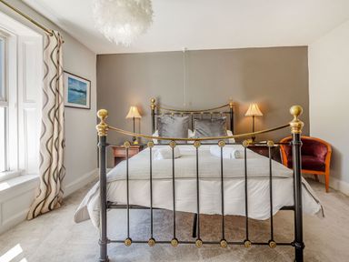 A bedroom with a metal bed frame two bedside tables with lamps a chair and a window with curtains at Bryn Rhosyn in Nefyn