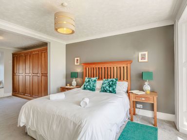 A bedroom with a wooden bed frame white bedding two green pillows bedside tables with lamps and a large wooden wardrobe at Bryn Rhosyn in Nefyn
