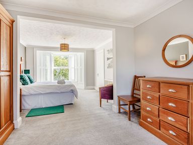 A bedroom with a bed near a window a wooden dresser with a round mirror a wooden chair and a purple armchair at Bryn Rhosyn in Nefyn
