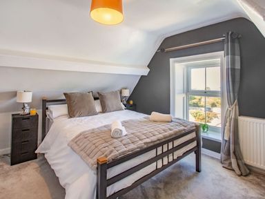 A bedroom with a double bed two bedside tables with lamps and drinks a window with curtains and a radiator Bryn Rhosyn in Nefyn