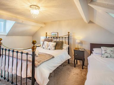 A bedroom with two beds a small bedside table with a lamp and a window at Bryn Rhosyn in Nefyn