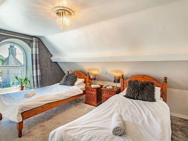 A bedroom with two wooden single beds white bedding gray pillows two bedside tables with lamps and a window with a view at Bryn Rhosyn in Nefyn