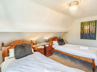 A bedroom with two wooden beds, white bedding, nightstands with lamps, and a forest picture on the wall at Bryn Rhosyn in Nefyn