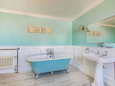 A bathroom with a blue clawfoot bathtub a white sink a radiator and three small paintings on the wall at Bryn Rhosyn in Nefyn