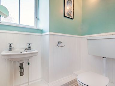 A small bathroom with a white sink and toilet and a frosted window at Bryn Rhosyn in Nefyn