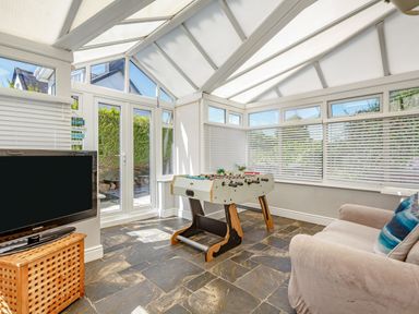 A conservatory with a foosball table sofa television and tiled floor at Bryn Rhosyn in Nefyn