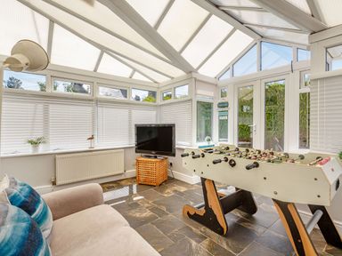 A conservatory with a foosball table television and sofa at Bryn Rhosyn in Nefyn