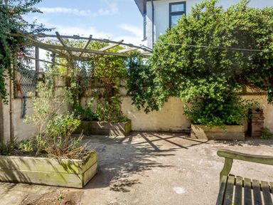 An outdoor patio area with wooden planters containing plants and a wooden pergola attached to a white brick wall at Bryn Rhosyn in Nefyn