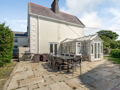 An outdoor patio with tables and chairs next to a white house with a conservatory at Bryn Rhosyn in Nefyn