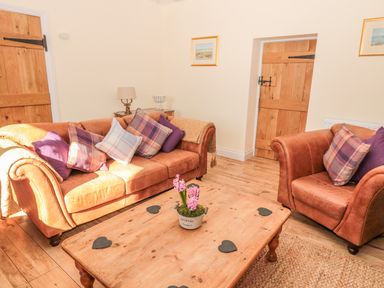 A living room with brown leather sofa and armchair pillows wooden coffee table and wooden doors at Baytree in Alnwick