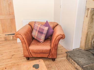 A brown leather armchair with two cushions in a room with wooden flooring and a stone fireplace at Baytree in Alnwick