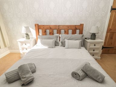 A bedroom with a wooden bed frame white bedding two bedside tables with lamps and rolled towels on the bed at Baytree in Alnwick