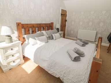 A bedroom with a wooden bed frame white bedside tables with lamps and rolled towels on the bed at Baytree in Alnwick