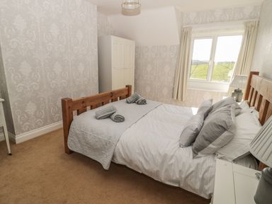 A bedroom with a wooden bed frame, striped bedding, folded towels, nightstands with lamps, a window with curtains, and a white wardrobe at Baytree in Alnwick