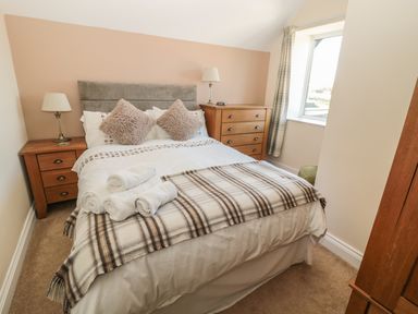 A bedroom with a double bed two bedside tables with lamps a chest of drawers and a window at Baytree in Alnwick