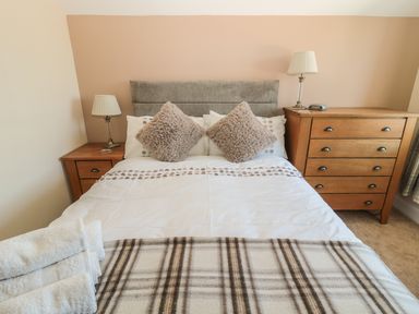 A bedroom with a double bed with two lamps on wooden bedside tables and a wooden dresser at Baytree in Alnwick